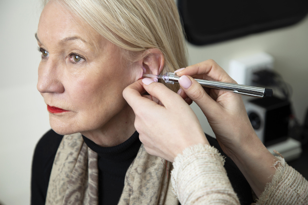 Audiologist examining the ear of a patient for a custom ear plug fitting.